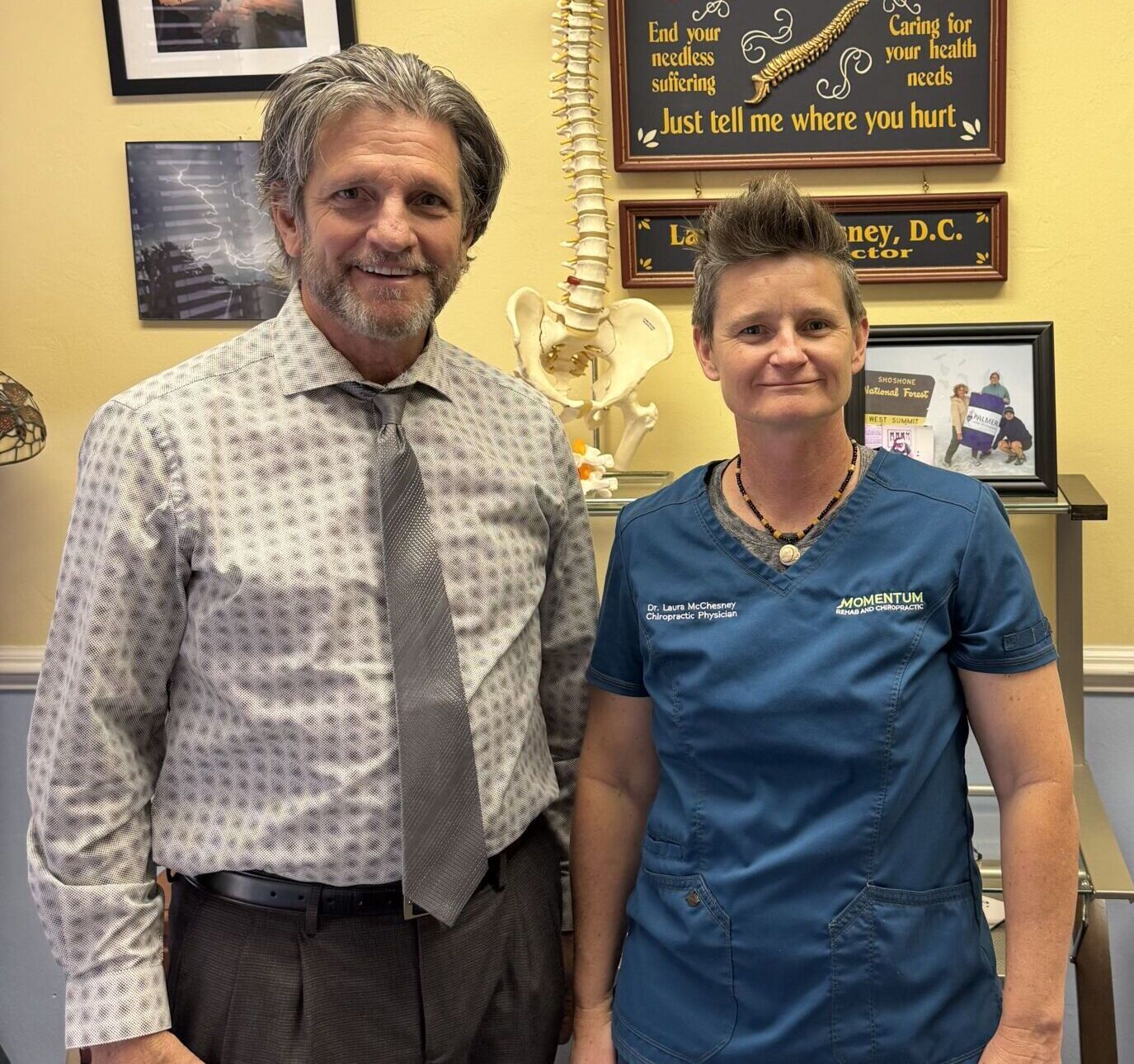 Photo of Gainesville Medical Injury Center: Momentum Rehab & Chiropractic's medical injury team, Dr. Kevin Huffman, DO (on the left) and Dr. Laura McChesney, DC (on the right), standing side by side, with arms by their sides and smiling.