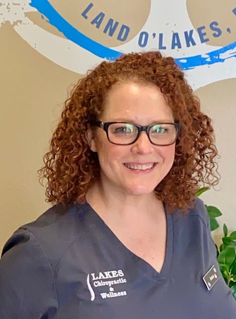 Profile picutre of Anna Chilton, a team member of Land O' Lakes Medical Injury Center, wearing glasses and a dark grey scrub top with practice logo on the front.