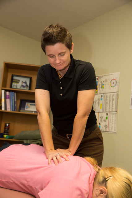 Dr. Laura McChesney, of Gainesville Medical Injury Center: Momentum Rehab & Chiropractic, performing an adjustment on a patient's back who is laying face down on the exam table.